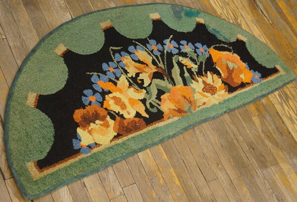 Semicircular rug with black, orange, and blue floral pattern and a green scalloped border on rustic wooden floor.