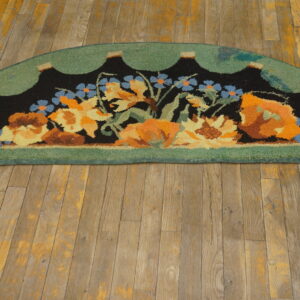 Semicircular high-pile rug features blue, orange, and yellow flowers on black with a scalloped green border on wood.