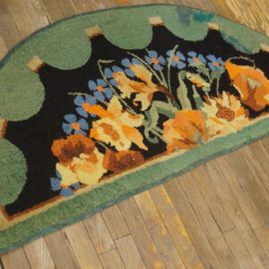 A half-round rug with orange, yellow, and blue flowers on a black field, bordered by green scallops, rests on distressed wood floor.