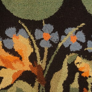 Textured pile rug detail showing blue, orange, and green floral motifs on a dark black ground.