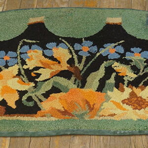 Hooked semicircular rug with orange and blue flowers on black, surrounded by a scalloped green border on wood planks.