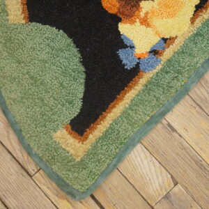 Looped, multi-colored rug corner in green, yellow, black, and blue rests on distressed diagonal wood planks.