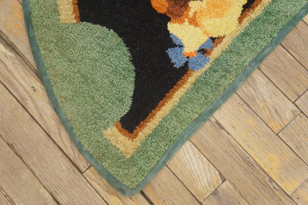 Looped, multi-colored rug corner in green, yellow, black, and blue rests on distressed diagonal wood planks.