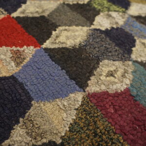 Multicolor coarse textured rug showing a dense geometric pattern of red, blue, black, and cream diamonds.