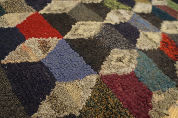 Multicolor coarse textured rug showing a dense geometric pattern of red, blue, black, and cream diamonds.