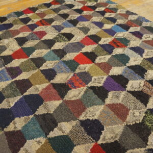 High-pile multicolored rug with a geometric cube patchwork design on wood planks.