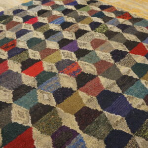 Textured multicolored rug featuring a geometric patchwork design of diamonds on rustic wood flooring.