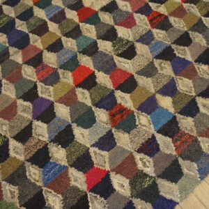 A multicolored rug with a dense, looped texture features an optical tumbling block pattern on wood floor.