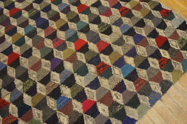 A multicolored rug with a dense, looped texture features an optical tumbling block pattern on wood floor.