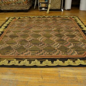 Dark olive and black geometric rug with a light green leaf border rests on aged wood planks.