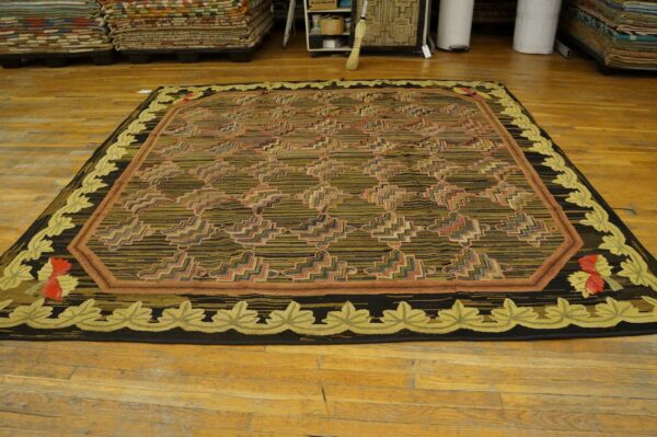 Dark olive and black geometric rug with a light green leaf border rests on aged wood planks.