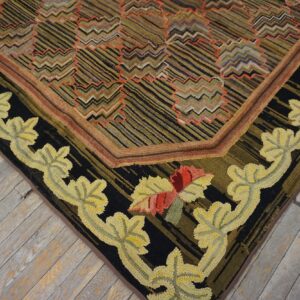 Close-up of a hooked rug on wood, featuring a black border with yellow leaves and a zigzag striped field.