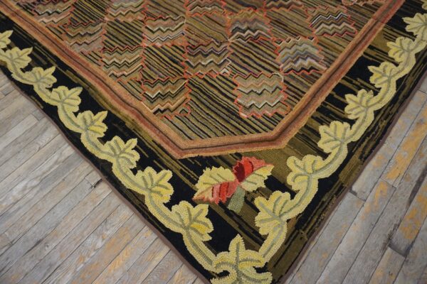 Close-up of a hooked rug on wood, featuring a black border with yellow leaves and a zigzag striped field.