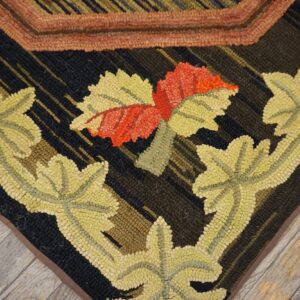 Hooked rug detail showing pale yellow and red florals against a dark ground, lying on light grey wood planks.