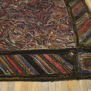 Multicolored hooked rug with dense swirling pattern, striped border, resting on worn wood floor.