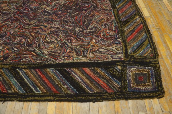 Multicolored hooked rug with dense swirling pattern, striped border, resting on worn wood floor.