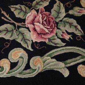 Black loop pile rug with a detailed floral pattern featuring a large pink rose and sage green scrolls.