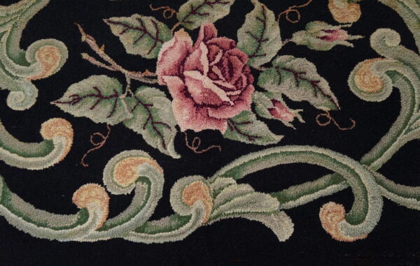 Black loop pile rug with a detailed floral pattern featuring a large pink rose and sage green scrolls.