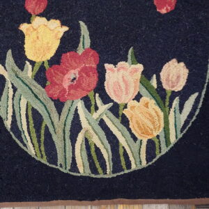 Floral hooked rug with red and yellow tulips on navy blue background, resting on worn wood flooring.