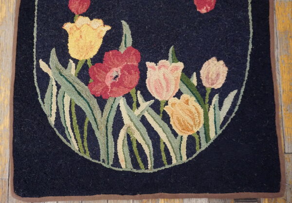 Floral hooked rug with red and yellow tulips on navy blue background, resting on worn wood flooring.
