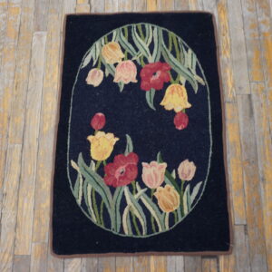 Dark blue rug displaying a centered oval floral design in red, pink, and yellow on distressed wooden floors.