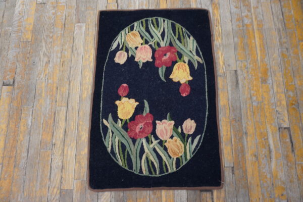 Dark blue rug displaying a centered oval floral design in red, pink, and yellow on distressed wooden floors.