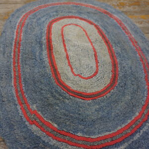 Textured blue and gray oval rug with red accent stripes placed on rustic wooden flooring.