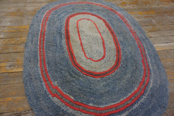 Textured blue and gray oval rug with red accent stripes placed on rustic wooden flooring.