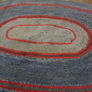 Shaggy round rug with concentric rings of blue, gray, and bright red resting on wood flooring.