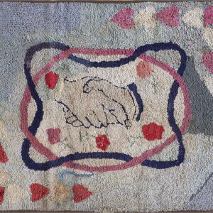 A bumpy, hooked rug in muted blue, cream, and pink features a central clasped handshake design.