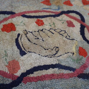 Textured, multi-colored rug featuring a central motif of two hands and scattered red floral accents on a wood floor.