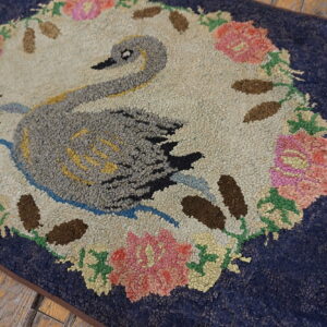 Textured navy blue rug features a gray swan and floral wreath pattern on rustic wood flooring.