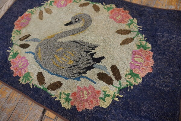 Textured navy blue rug features a gray swan and floral wreath pattern on rustic wood flooring.