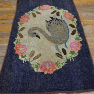 A textured navy blue rug featuring a gray swan and pink floral wreath on distressed yellow wood floors.