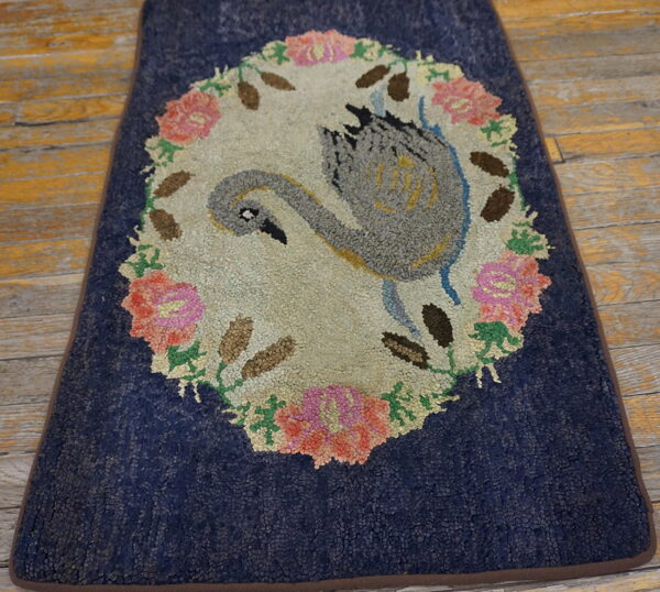 A textured navy blue rug featuring a gray swan and pink floral wreath on distressed yellow wood floors.