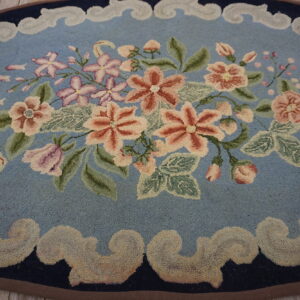 Oval blue rug featuring a central bouquet of peach and pink flowers, bordered by scrolling beige motifs on wood planks.