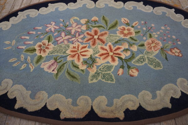 Oval blue rug featuring a central bouquet of peach and pink flowers, bordered by scrolling beige motifs on wood planks.