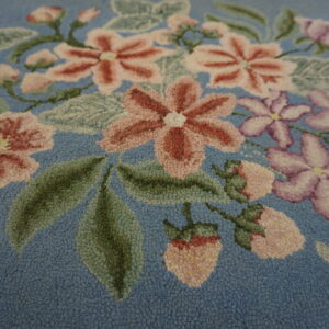 Highly textured floral rug detail showing pink, lavender, and green motifs on a dusty blue background.