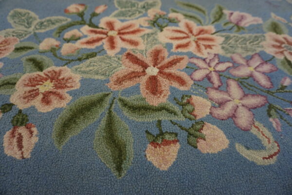 Highly textured floral rug detail showing pink, lavender, and green motifs on a dusty blue background.