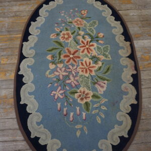 Hooked oval rug featuring a pink floral bouquet and scrolled border on a weathered wood floor.