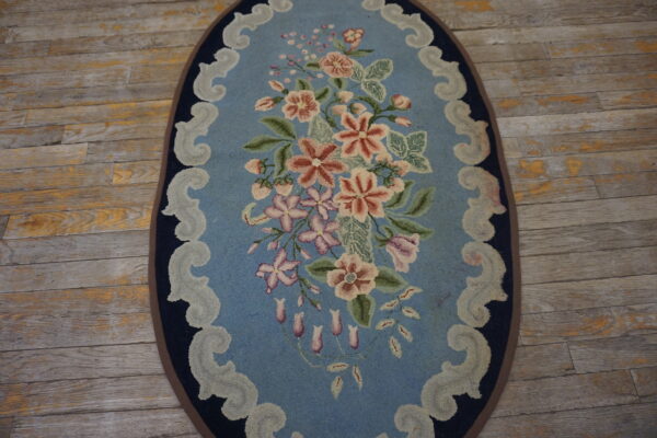 Hooked oval rug featuring a pink floral bouquet and scrolled border on a weathered wood floor.