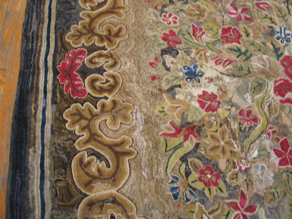Close-up of a textured rug with a tan scroll border and multicolored floral pattern on hardwood floor.