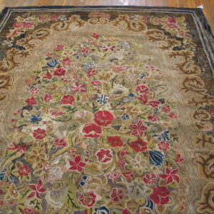 An ornate, multi-color floral rug with a sculpted border rests on wide plank wood flooring.