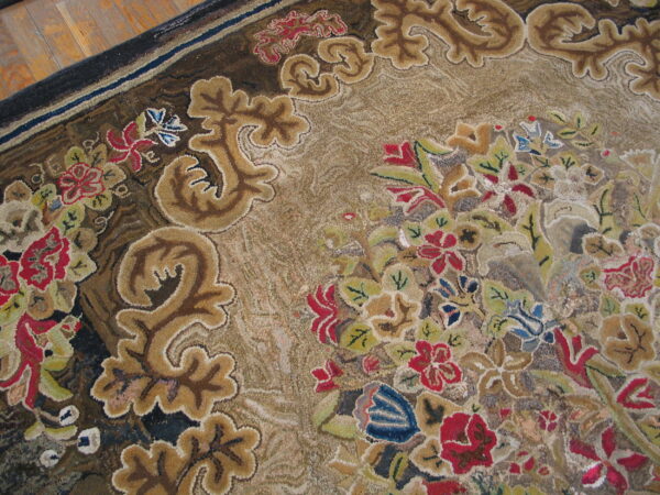 Textured, low-pile rug displaying intricate floral and baroque scroll patterns in muted tan, red, blue, and brown tones.