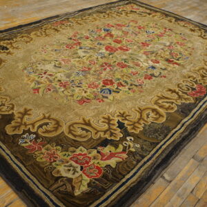 Textured tan rug with a multicolored floral design and ornate gold and dark brown scrolling borders on wood floorboards.