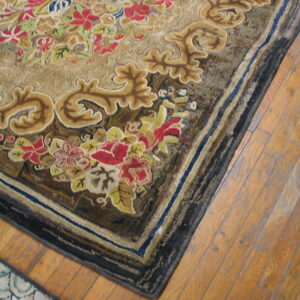 Detailed view of a tan rug featuring sculpted red floral and gold scrollwork motifs on light wood plank flooring.