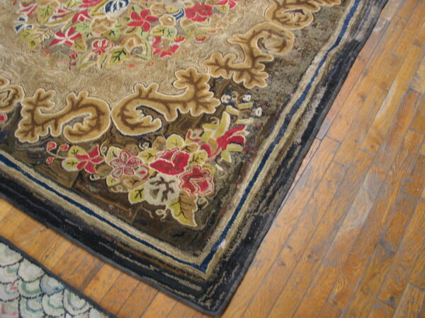 Detailed view of a tan rug featuring sculpted red floral and gold scrollwork motifs on light wood plank flooring.