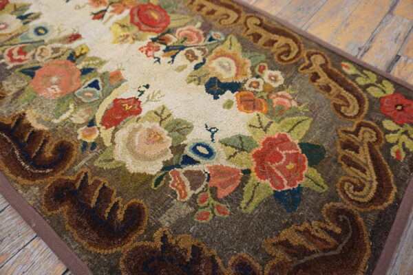 A looped pile rug with a colorful floral center and a dark brown scrolling border rests on wood planks.