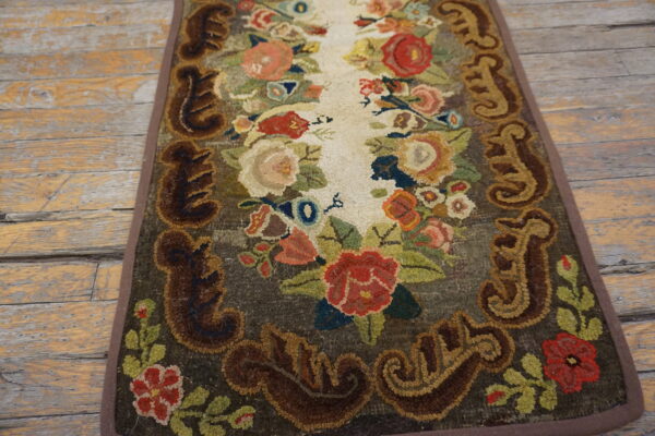Hooked floral runner rug with a multicolored pattern and dark scrolled border on weathered wooden planks.