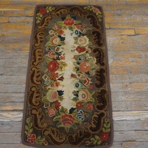 Highly textured floral runner rug with vibrant colors and dark scrolled borders rests on distressed wood flooring.